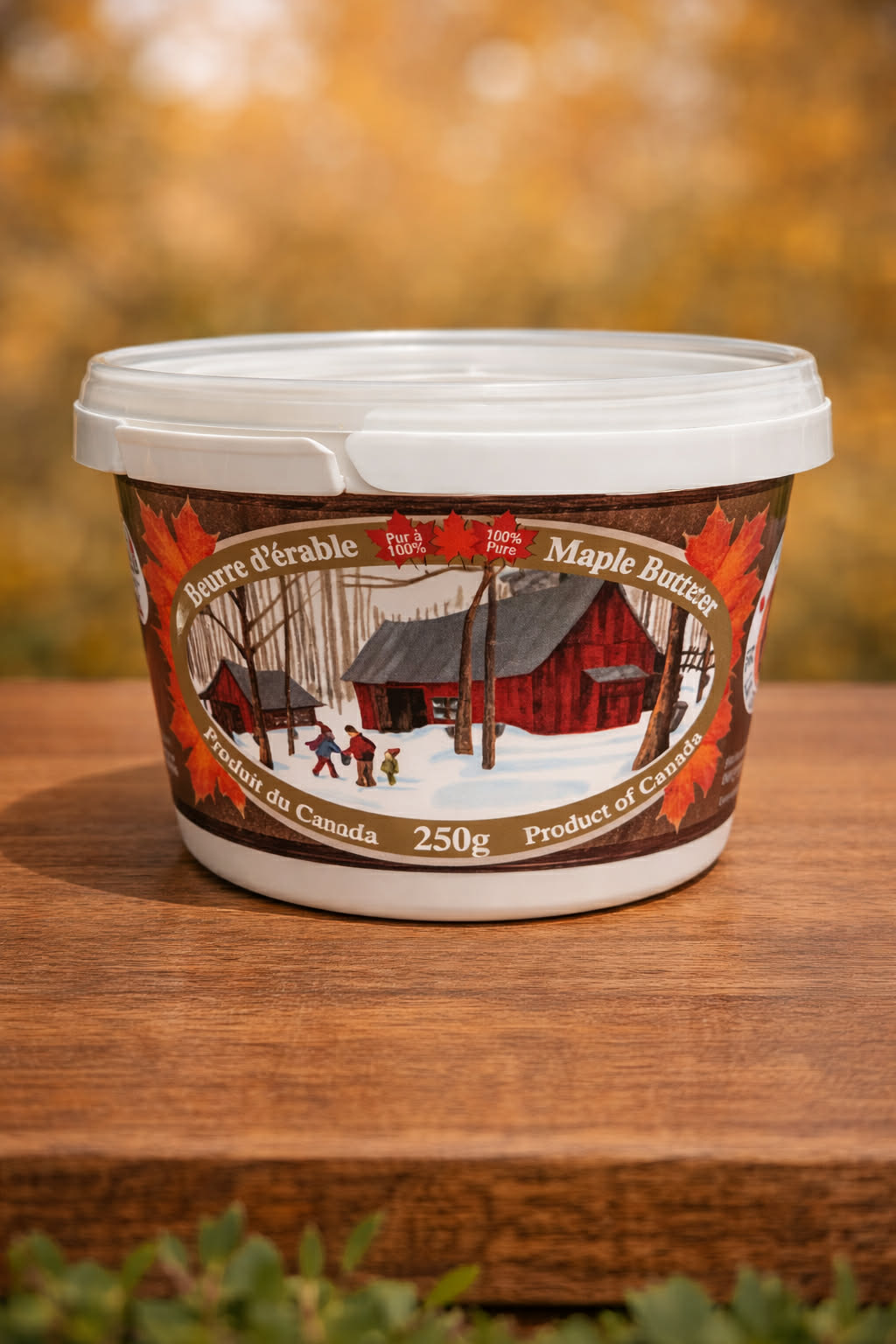 Container of maple butter with a rustic cabin design on a wooden surface
